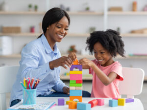 Adorable Black Kid And Child Development Specialist Playing With